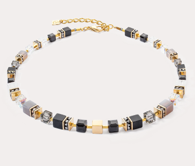 GeoCUBE® Precious statement ketting in goud en zwart: tijdloze verfijning in zwart Voor wie tijdloze elegantie waardeert, is de GeoCUBE® Precious statement ketting in goud en zwart de perfecte keuze. Ook de grote GeoCUBES® van kostbare edelstenen en glinsterende Swarovski-kristallen® staan centraal in dit sieraad. De opstelling van de kubussen, die naar achteren toe kleiner worden, zorgt voor een harmonieus ontwerp en een optimaal draagcomfort. De gouden roestvrijstalen kubus in het midden van de ketting zorgt voor een stralend accent en benadrukt op elegante wijze het diepe zwart van de edelstenen. Deze ketting is een echte klassieker die elke feestelijke outfit compleet maakt met een vleugje luxe verfijning.