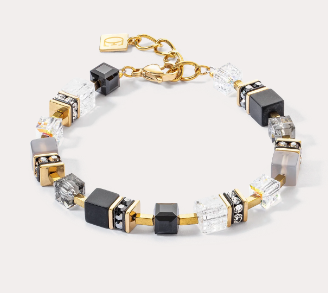 GeoCUBE® Precious statement armband in goud en zwart: klassieke elegantie in zwart De GeoCUBE® Precious statement armband in goud en zwart is een meesterwerk van tijdloze elegantie. De kleinere GeoCUBES® van edelstenen en glinsterende Swarovski-kristallen® passen perfect bij elkaar en creëren een harmonieus ontwerp dat zowel subtiel als effectief is. Deze armband is de perfecte aanvulling op de bijpassende ketting en voegt een stijlvol accent toe dat elke outfit een luxe touch zal geven.