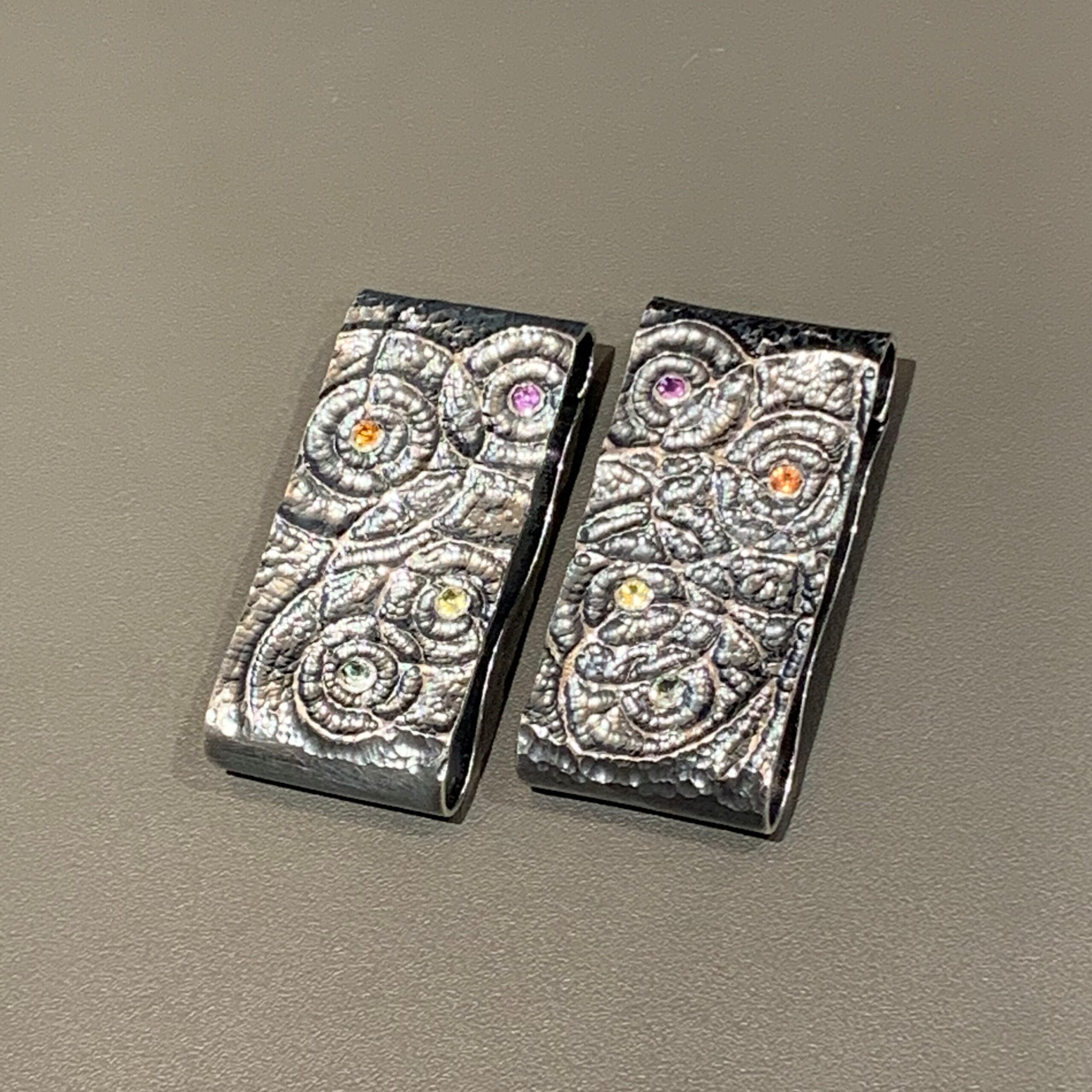 Inovative &Auml;rmelklammer "Hemdheld". Ziseliertes Silber, geschw&auml;rzt mit 8 farbigen Safiren. F&uuml;r dunkle und/oder floral gemusterte Hemden oder &Auml;rmelaufschl&auml;ge besonders geeignet. - UNIKAT