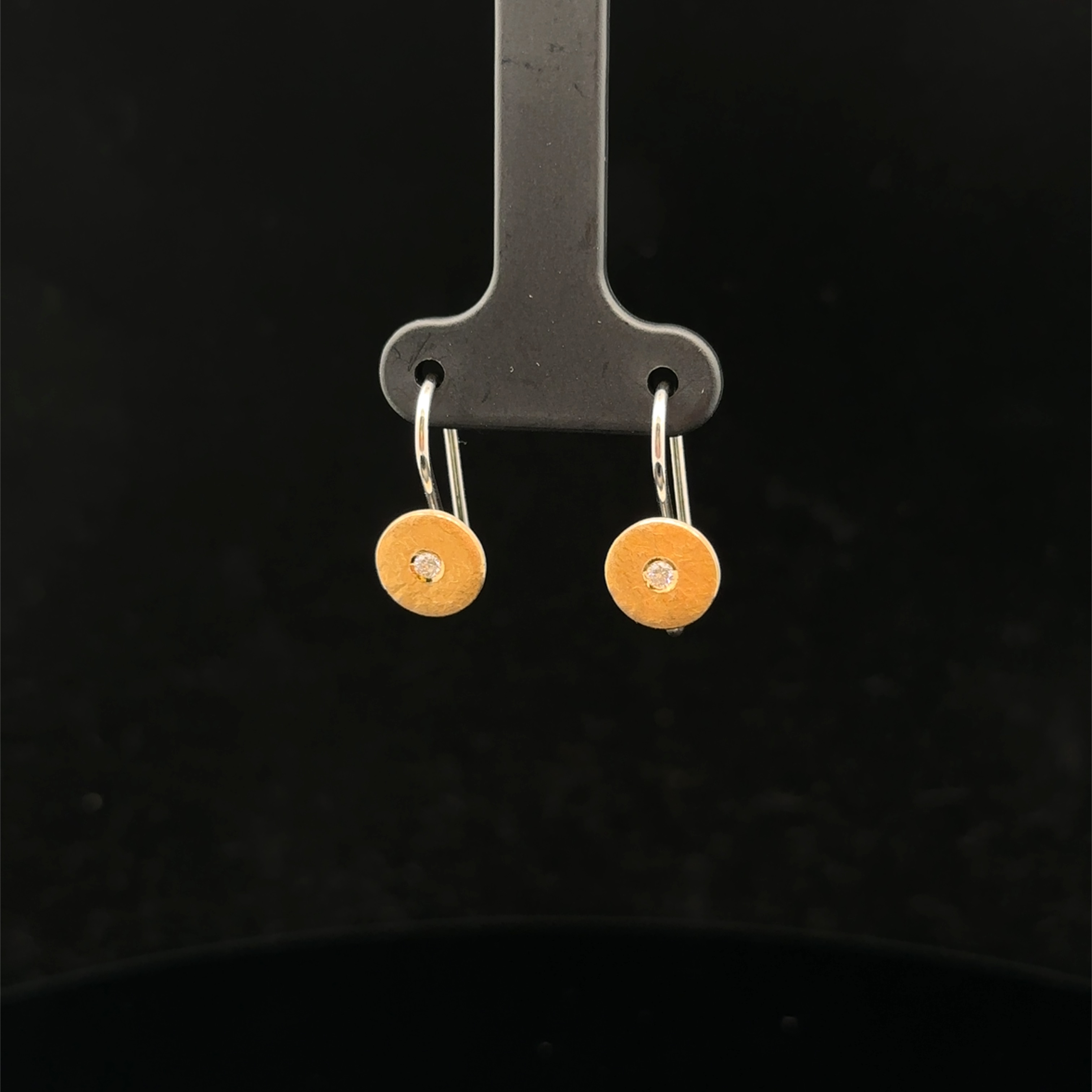 Diese eleganten Ohrhänger mit Haken und kleinen Scheiben verfügen über zwei 0,03 Karat Brillanten in Silber-Feingold. Sie sind zeitlos und vielseitig und eignen sich perfekt für jeden Anlass. Tragen Sie diese wunderschönen Ohrringe einzeln für einen subtilen Look oder kombinieren Sie sie mit anderen Schmuckstücken für einen edlen und funkelnden Auftritt.