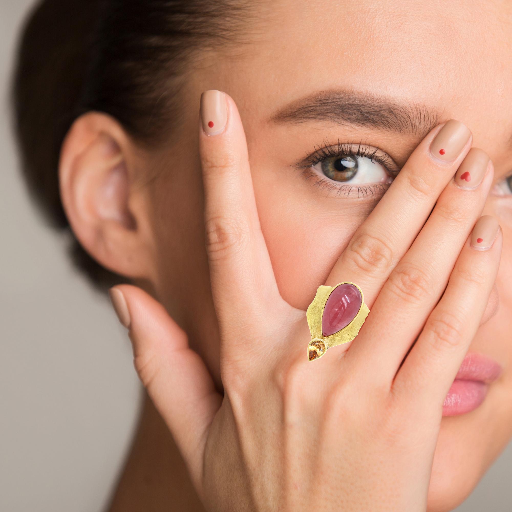 Der Ring besteht aus Gelbgold 750/ooo und ist mit den Edelsteinen Rhodochrosit als Cabochon und einem Mandaringranat Tropfen mit 1,26ct gefertigt. Es handelt sich um ein UNIKAT. Die Oberfläche ist mit einer Schweißstruktur versehen. Tragen Sie ihn am besten am Mittelfinger für einen eleganten und stilvollen Auftritt. Ein zeitloses Schmuckstück für jeden Anlass.