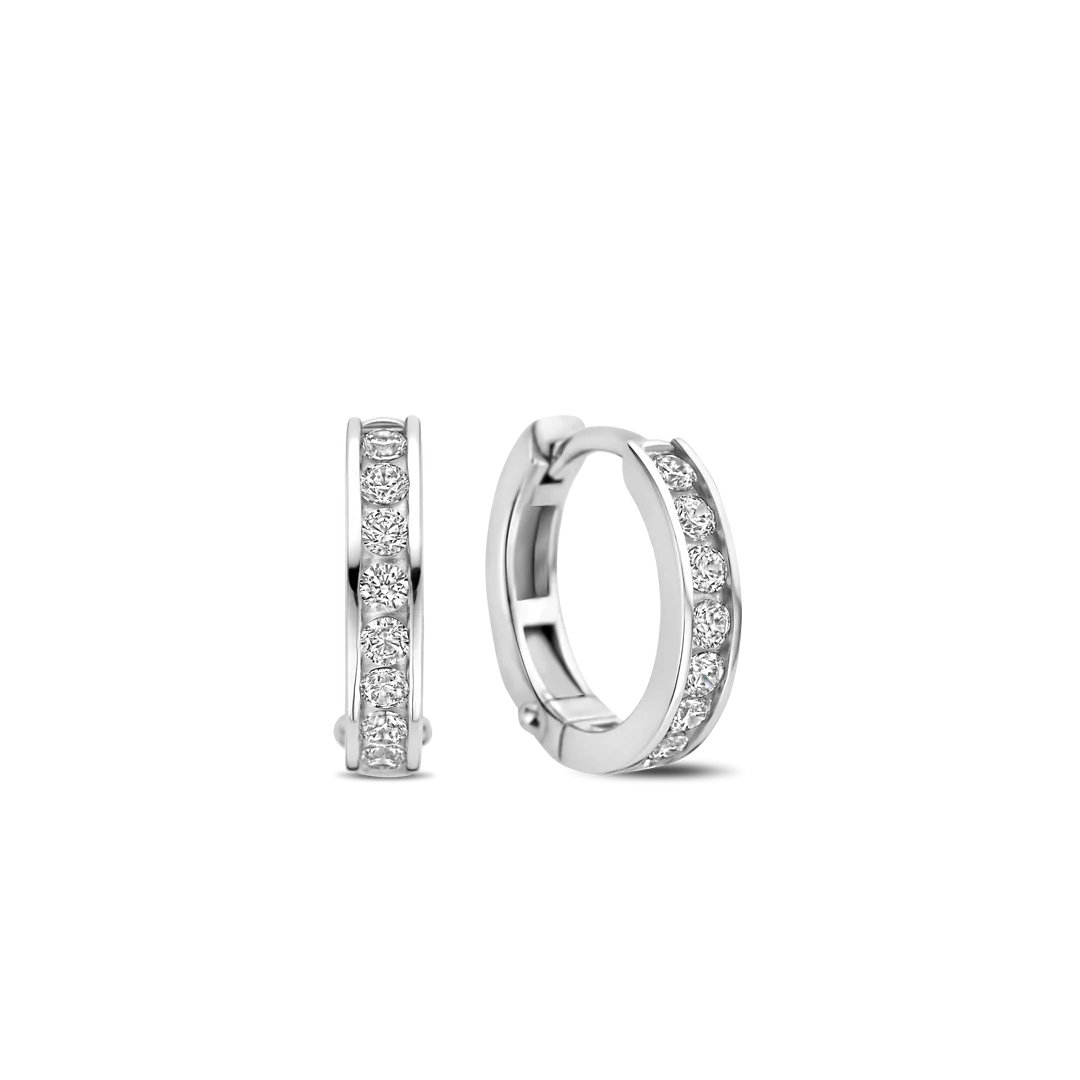Hul jezelf met moderne elegantie met de TI SENTO Pave Silver Hoop Earrings 7973ZI. Gemaakt van 925 sterling zilver en verzilverd voor blijvende schittering, hebben deze oorbellen twee kleine hoepels versierd met een verblindende rij rechthoekig geslepen witte cubic zirconia stenen. De geometrische vorm van de stenen voegt een vleugje gedurfde verfijning toe aan het klassieke hoepelontwerp. Dit paar oorbellen is een bewijs van de kunst van fijne sieraden, met een harmonieuze mix van traditie en moderniteit. Het koele zilver en de sprankelende cubic zirconia stenen creëren een betoverend spel van licht en textuur. Verhoog je dagelijkse look met deze delicate minimalistische stukken. Draag ze alleen voor een minimalistische uitspraak of gecombineerd met andere TI SENTO oorbellen voor een gepersonaliseerde touch die vertrouwen en aantrekkingskracht uitstraalt. Laat deze oorbellen de vonk zijn die je innerlijke uitstraling ontsteekt. Met zorg vervaardigd voor gevoelige huid, zorgen deze nikkelvrije en hypoallergene oorbellen voor langdurig comfort en kwaliteit.


