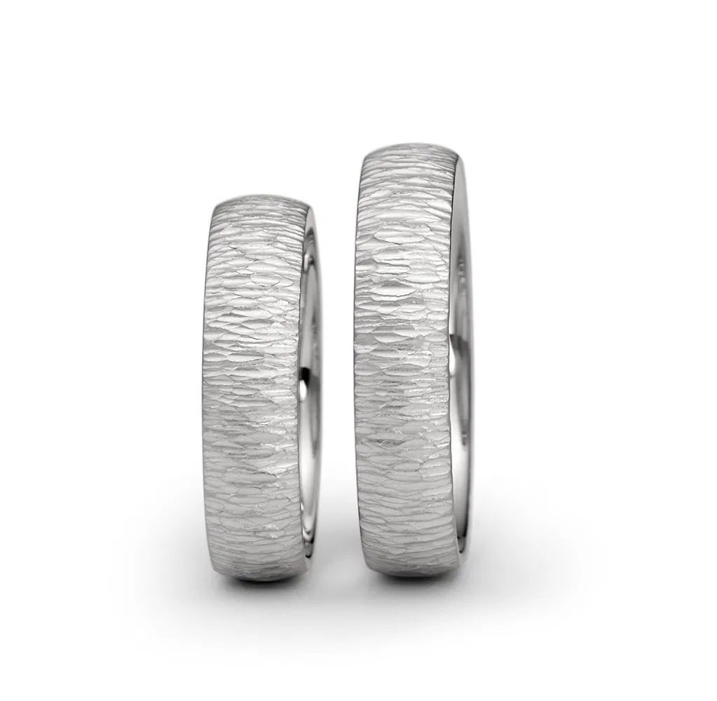 een 18 krt witgouden ring van Niessing Linear met hammerslag motief erop. 
ring is 5 mm breed