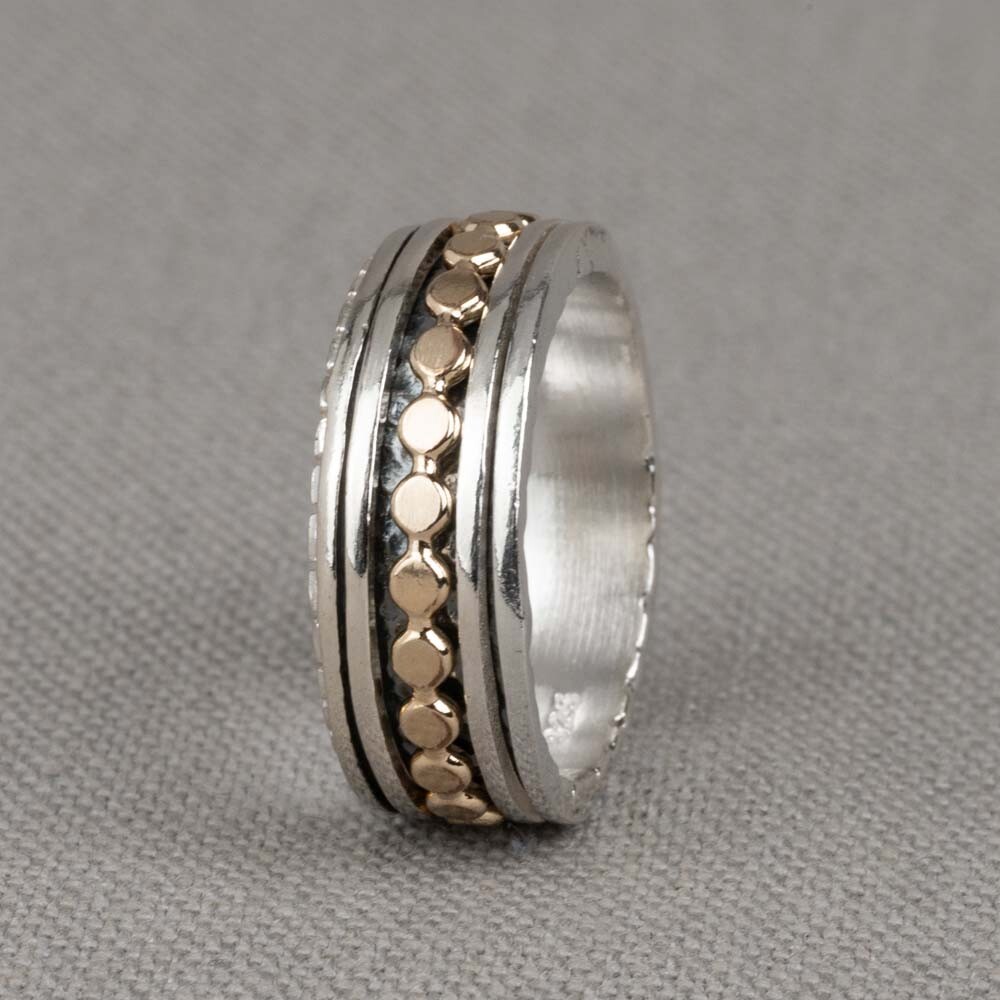 Deze ring is gemaakt van 925 sterling zilver en gold filled. De ring heeft drie losse ringetjes die afzonderlijk van elkaar kunnen bewegen. De ringetjes bestaan uit twee zilveren en één gold filled ringetje in de vorm van platte balletjes. De onderkant van de ring is geoxideerd wat zorgt voor extra diepte. 