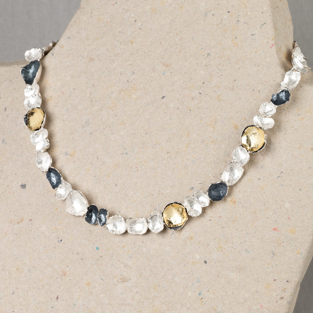 Collier gemaakt van 925 sterling zilver, geoxideerd zilver en zilver verguld. Dit schakelcollier is door de drie kleuren en verschillende organische schaaltjes een echt Jeh collier.