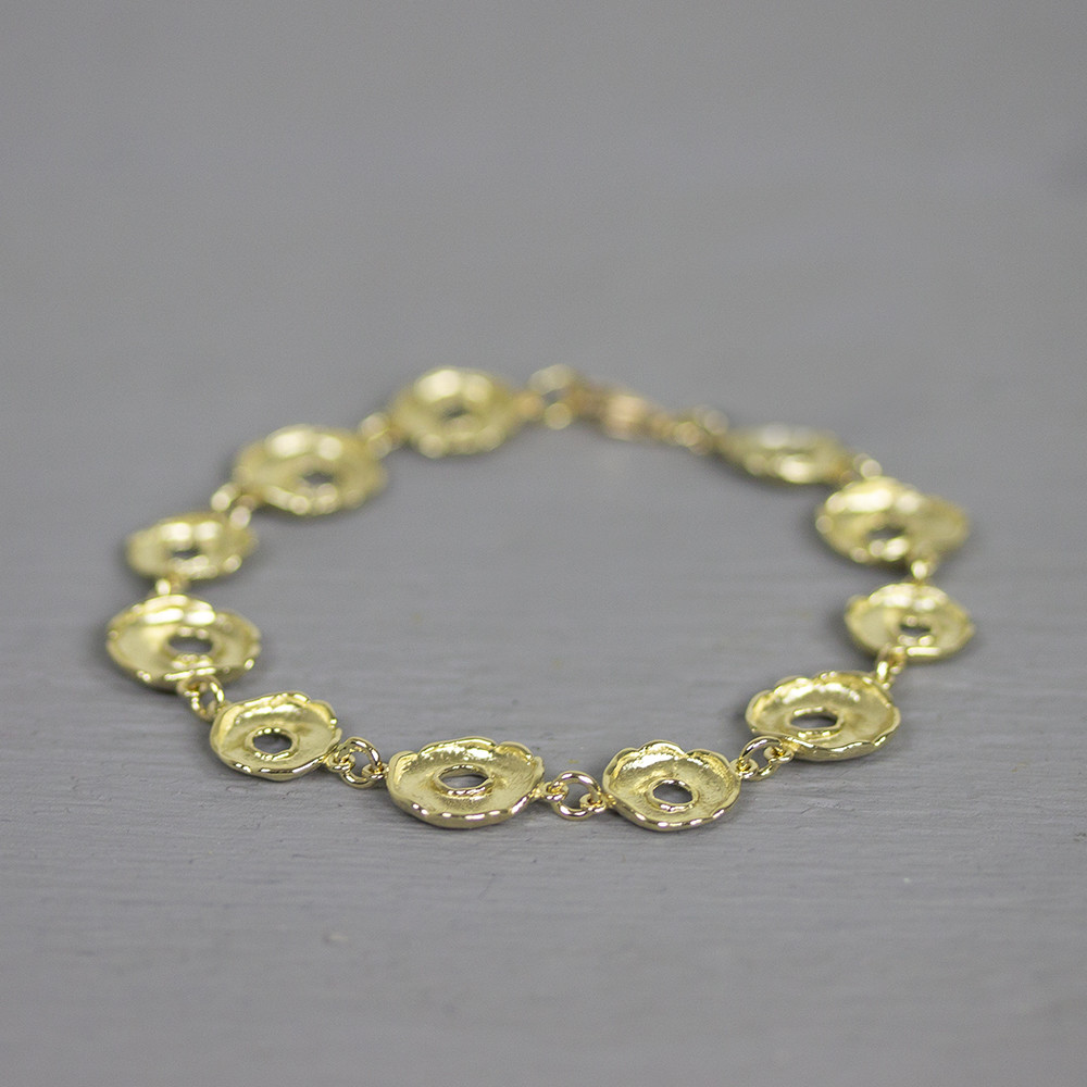 Armband gemaakt van 14 karaat met schakels in de vorm van een donut. De gouden sieradenlijn van Jeh is gemaakt van 14 karaats goud. Dit karaatgehalte wordt in Nederland het meest gebruikt, vanwege de hardheid en de kleur. Puur goud is te zacht om draagbare sieraden van te maken, daarom worden er bij metalen gebruikt. Vaak wordt er zilver en koper gebruikt zodat je kunt blijven spreken van 'edele metalen'. Bij 14 karaat goud zijn er van de 1000 delen, 585 delen puur goud. De overige 415 delen bestaan dus uit de overige metalen.