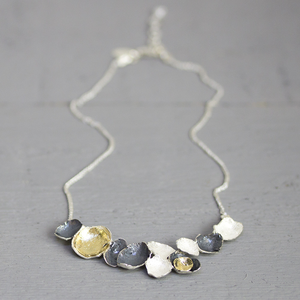 Collier gemaakt van 925 geoxideerd sterling zilver, met in het midden een hanger van geoxideerd zilver en zilver verguld. De boog van schakels zijn net kleine kommetjes.
\nDe lengte van het collier is 42 cm.