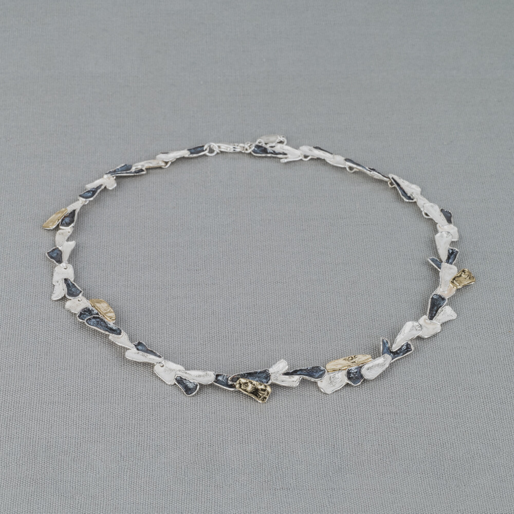 Collier gemaakt van 925 (geoxideerd) sterling zilver en zilver verguld. Dit schakelcollier is door de drie kleuren en verschillende organische schaaltjes een echt Jéh collier. Combineer met een mooie armband en oorbellen voor een complete look!