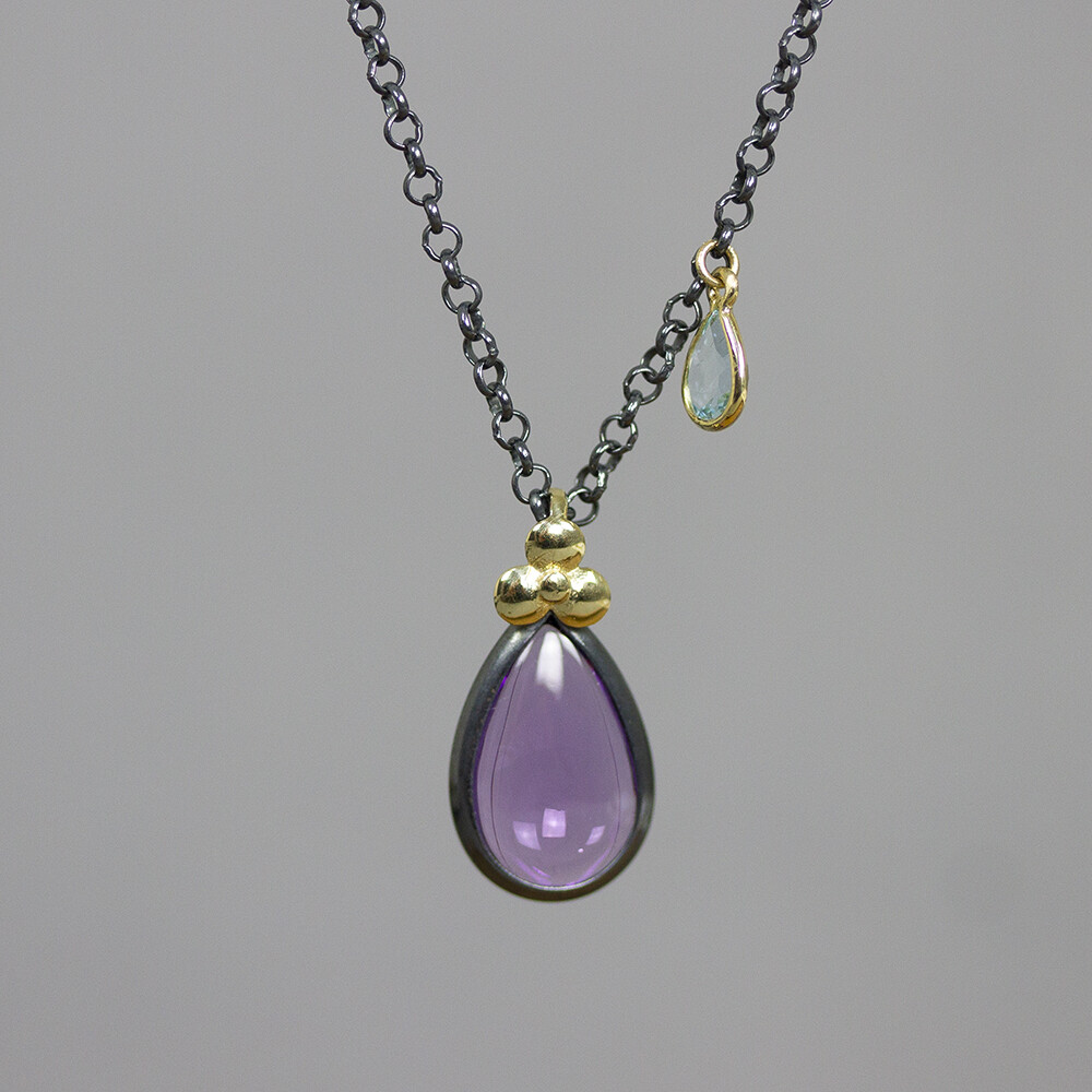 Collier gemaakt van 925 geoxideerd sterling zilver, met als grote edelsteen een Amethist en een kleine Blauwe Topaas. Boven de hanger zit een klavertje 3 van 14 karaat goud. Let op het model draagt dit collier in chocolade maansteen.