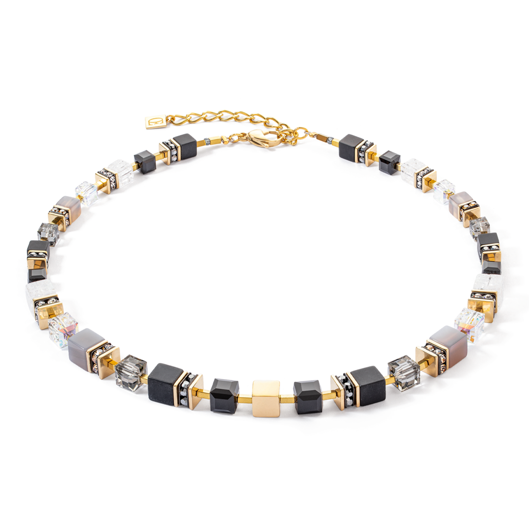 GeoCUBE® Precious statement necklace in goud en zwart: tijdloos raffinement in zwart Voor wie van tijdloze elegantie houdt, is de GeoCUBE® Precious statement necklace in goud en zwart de perfecte keuze. De grote GeoCUBES® van kostbare edelstenen en glinsterende Swarovski®-kristallen staan ook in dit sieraad centraal. De opstelling van de kubussen, die naar achteren toe kleiner worden, zorgt voor een harmonieus ontwerp en optimaal draagcomfort. Het gouden roestvrijstalen blokje in het midden van de ketting zorgt voor een stralend accent en accentueert op elegante wijze het diepzwarte van de edelstenen. Deze ketting is een echte klassieker die elke feestelijke outfit afmaakt met een vleugje luxueuze verfijning.

De materialen van de ketting zijn Agaat, Onyx, Bergkristal, Swarovski®, Kristallen, Strass rondellen, Roestvrij staal goud. De sluiting is gemaakt van goud roestvrij staal. De lengte van de ketting is 45 cm + 6 cm verlenging.