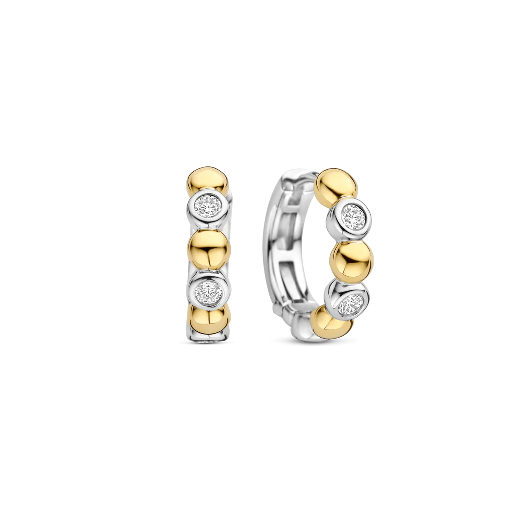 Deze TI SENTO oorbellen 78008ZY combineren gedurfd contrast met verfijnde elegantie. Gemaakt van 925 sterling zilver en verguld, tonen deze oorbellen een opvallend samenspel van bezel gezette cubic zirconia stenen en gepolijste goudkleurige kralen, wat zorgt voor een dynamisch ritme van licht en textuur. Deze oorbellen voegen een warme, zonovergoten gloed toe aan elke look. De veilige scharnier sluiting zorgt voor een comfortabele pasvorm, waardoor ze veelzijdig zijn voor dag en nacht, of ze nu solo worden gedragen of in combinatie met andere favorieten. Nikkelvrij en hypoallergeen voor luxueus comfort. Een mix van gouden straling en fonkelende schittering, deze hoepels stralen een verfijnde maar speelse charme uit die je oren direct verfraait.

