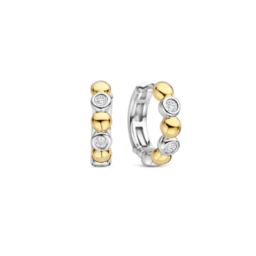 Deze TI SENTO oorbellen 78008ZY combineren gedurfd contrast met verfijnde elegantie. Gemaakt van 925 sterling zilver en verguld, tonen deze oorbellen een opvallend samenspel van bezel gezette cubic zirconia stenen en gepolijste goudkleurige kralen, wat zorgt voor een dynamisch ritme van licht en textuur. Deze oorbellen voegen een warme, zonovergoten gloed toe aan elke look. De veilige scharnier sluiting zorgt voor een comfortabele pasvorm, waardoor ze veelzijdig zijn voor dag en nacht, of ze nu solo worden gedragen of in combinatie met andere favorieten. Nikkelvrij en hypoallergeen voor luxueus comfort. Een mix van gouden straling en fonkelende schittering, deze hoepels stralen een verfijnde maar speelse charme uit die je oren direct verfraait.