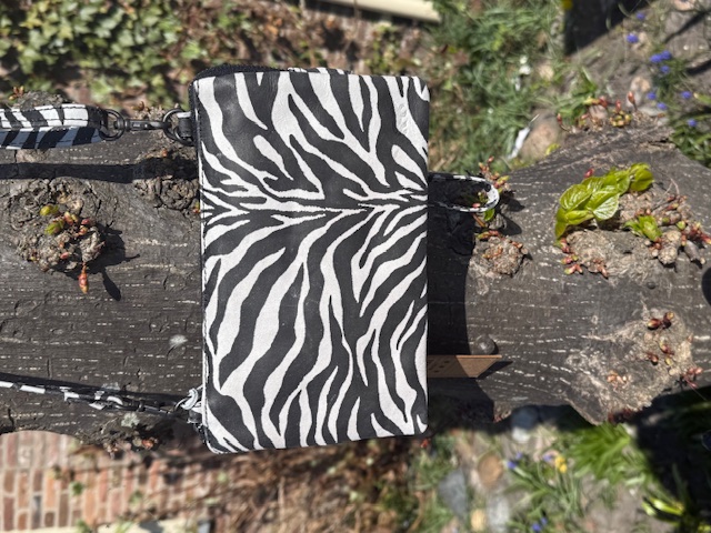 Een schoudertas welke ook als grote Clutch/portemonnee kan worden gebruikt. Onder de toprits bevinden zich drie vakken waarvan het middelste vak is uitgerust om ook pasjes in op te bergen. Verder is het tasjes voorzien van een lange afneembare schouderriem en een afneembaar polsbandje. Afmetingen: Hoogte 14cm x breed 22cm x diep 5cm