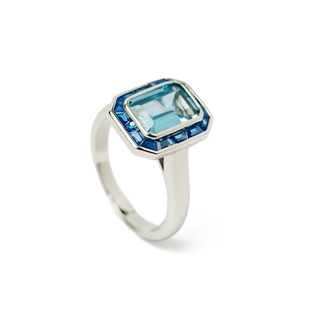 Ring with blue emerald-cut stones. This ring stands out for its emerald-cut blue topaz, surrounded by a halo of baguette sapphires set in a silver setting. Its modern and elegant finish makes it the ideal piece of jewelry for special occasions, combining luxury and distinction in every detail.