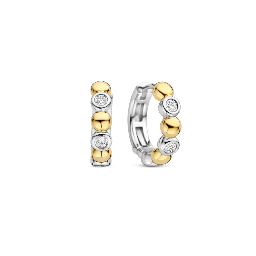 Deze TI SENTO oorbellen 78008ZY combineren gedurfd contrast met verfijnde elegantie. Gemaakt van 925 sterling zilver en verguld, tonen deze oorbellen een opvallend samenspel van bezel gezette cubic zirconia stenen en gepolijste goudkleurige kralen, wat zorgt voor een dynamisch ritme van licht en textuur. Deze oorbellen voegen een warme, zonovergoten gloed toe aan elke look. De veilige scharnier sluiting zorgt voor een comfortabele pasvorm, waardoor ze veelzijdig zijn voor dag en nacht, of ze nu solo worden gedragen of in combinatie met andere favorieten. Nikkelvrij en hypoallergeen voor luxueus comfort. Een mix van gouden straling en fonkelende schittering, deze hoepels stralen een verfijnde maar speelse charme uit die je oren direct verfraait.