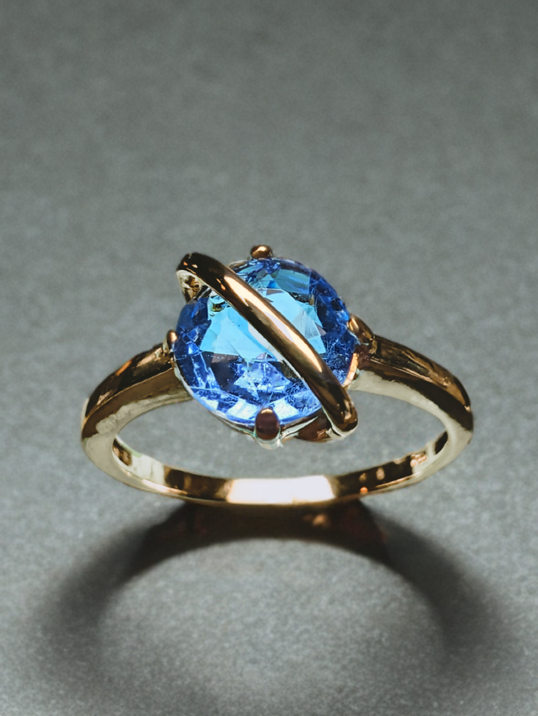 Een bijzondere 14 Karaat Geel gouden Ring met een briljant geslepen synthetische aquamarijn.
De beugel over de steen staat niet alleen speels, maar beschermd de steen tevens tegen stoten.

De ring en steen hebben lichte draagschade, maar zijn; ultrasonisch gereinigd, gepolijst en de zetting is zo goed als mogelijk nagekeken.

Op Vintage ringen kunnen wij maar een beperkte garantie geven. 
Dit omdat wij niet de exacte geschiedenis en fabricatie methode van de ring kunnen weten.