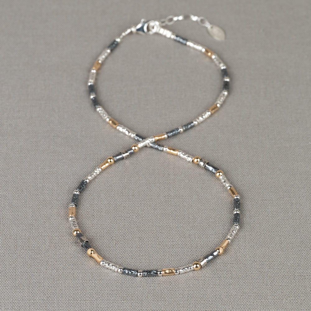 Collier gemaakt van 925 sterling zilver, geoxideerd zilver en goldfilled. Dit collier is een uitbreiding op de 17708. De drie metaalsoorten komen afwisselnd terug en zijn bewerkt met een lichte hamerslag. Over een aantal schakels zit een beweegbaar zilver bandje, dit cree&euml;rt een speels effect. Lengte 46.5 cm