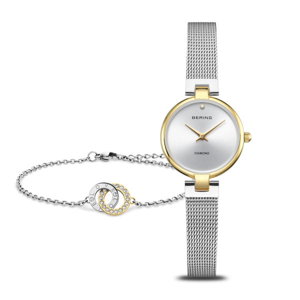  Vier 15 jaar BERING met deze exclusieve jubileumset, geïnspireerd door de heldere schoonheid van de Noordpool en het minimalistische Scandinavische design. De set bestaat uit een elegant BERING dameshorloge en een perfect bijpassende armband – een stijlvolle combinatie van tijdloze elegantie en symbolische betekenis.  Het horloge is voorzien van een zilverkleurige Milanese armband en goudkleurige details op de kast en wijzers – een subtiel hoogtepunt voor dagelijks gebruik en speciale gelegenheden. De bijpassende armband heeft twee in elkaar verstrengelde ringen: een in gepolijst roestvrij staal en een bezet met schitterende stenen – als teken van verbondenheid en eeuwigheid.  Deze BERING jubileumset combineert hoogwaardig design en bijzondere symboliek. Hij wordt geleverd in een elegante geschenkverpakking – ideaal als cadeau of als exclusieve herinnering aan het 15-jarig bestaan van BERING. 