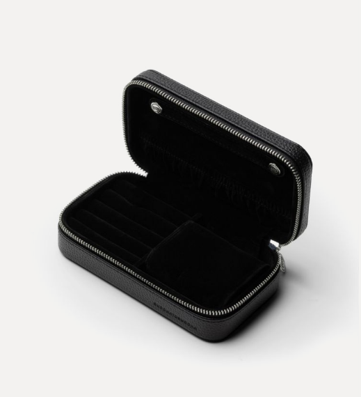 De Jewelry Travel Case Black Medium biedt een luxueuze en praktische manier om je sieraden overzichtelijk te bewaren, zowel thuis als onderweg. In de flap bevindt zich een afneembare strip met drukknopen voor het opbergen van 5 paar oorbellen, terwijl kettingen eromheen gehangen kunnen worden. Onderin biedt de case aan de linkerkant ruimte voor meerdere ringen, oorbellen en hangers, terwijl de rechterkant een uitneembare armband-rol bevat, ideaal voor meerdere armbanden. Voor grotere armbanden kan de armband-rol worden verwijderd om extra ruimte te creëren. De case is gemaakt van RCS-gecertificeerd gerecycled PU en de voering van GRS-gecertificeerd gerecycled polyester. De duurzame sieradenetui is afgewerkt met een zilverkleurige BTB-ritssluiting en BUDDHATOBUDDHA logo’s die in reliëf zijn aangebracht.