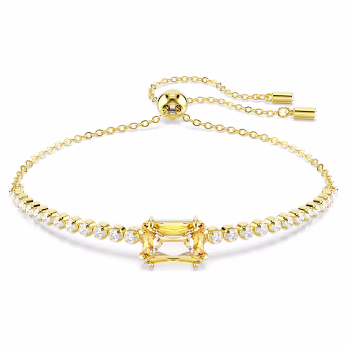 Deze klassieke Tennis-armband voegt een vleugje glans toe aan elke look. Het sieraad met goudkleurige toplaag en schuifsluiting voor een verstelbare pasvorm heeft een gelijkmatige rij Swarovski Zirkonia en wordt geaccentueerd door een caramelkleurige Swarovski Zirkonia in baguette-slijpvorm in het midden. Hiermee geeft u een levendige draai aan een tijdloze stijl die u keer op keer kunt dragen.