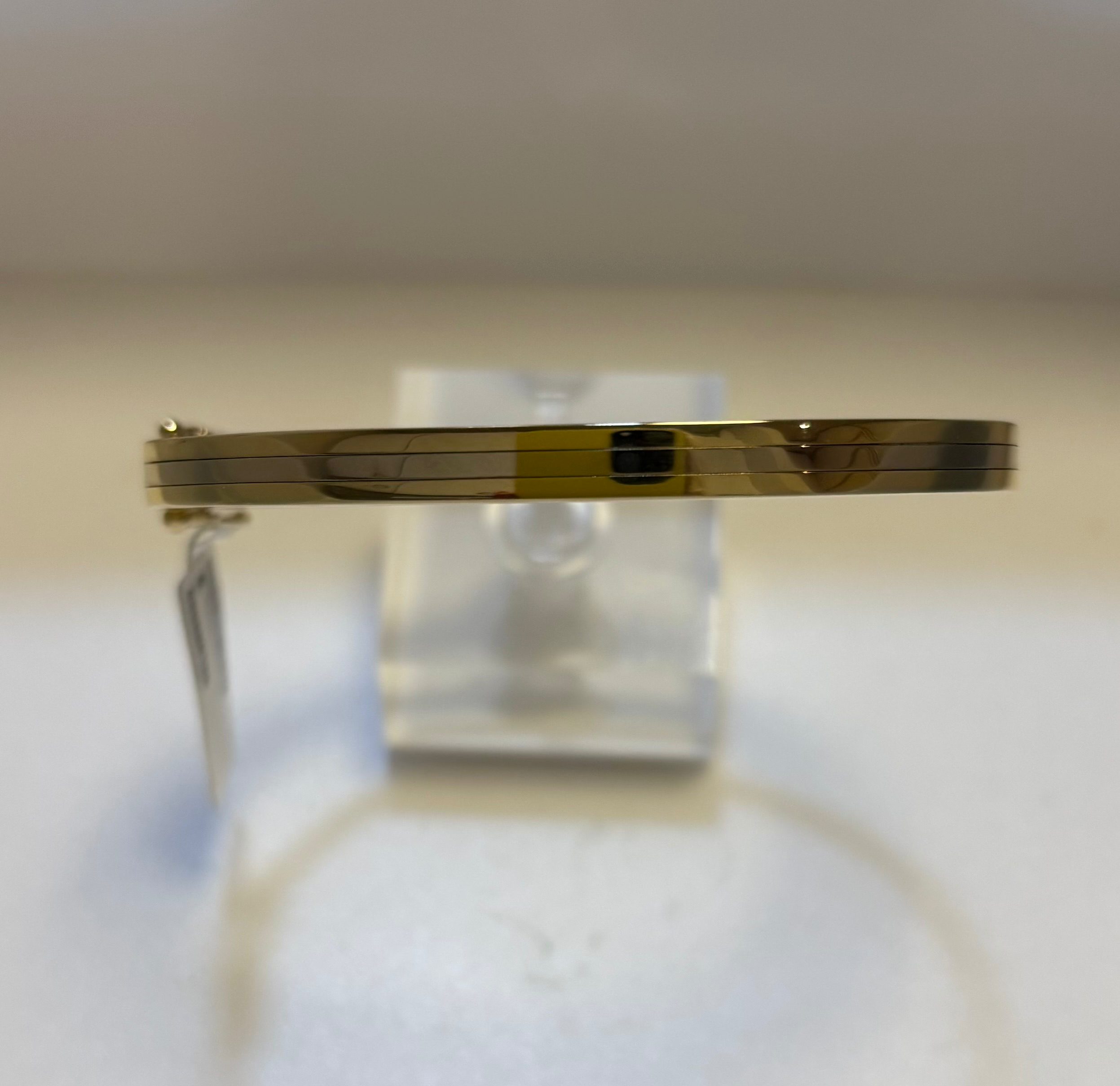 Bicolour gladde bangle armband. De buitenbanen zijn geel, de middenbaan is wit. Met scharnier, baksluiting en 2x vh8. 
Doorsnede; 61 mm
Breedte; 5 mm