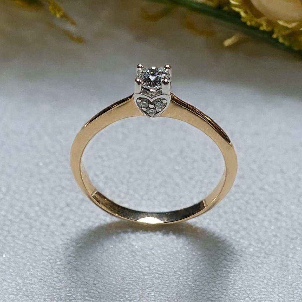 14k geelgouden ring met een, briljant geslepen, diamant gezet in een witgouden chaton met vier zetpoten. De chaton is aan beide kanten versierd met een hart met daarin drie, briljant geslepen, diamant. Alle Diamanten zijn van natuurlijke oorsprong.