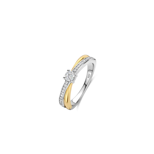 Ervaar het betoverende samenspel van licht en schaduw met deze TI SENTO goudkleurige ring 12374ZY. Dit verfijnde stuk, vervaardigd uit 925 zilver, heeft twee verstrengelde banden: één goud gekleurd, de andere schitterend met een fonkelende pavé van witte zirkonia. In het hart van dit betoverende ontwerp wordt een briljante zirkonia getoond in een delicate prongzetting, die het licht vangt en een vleugje tijdloze elegantie toevoegt.