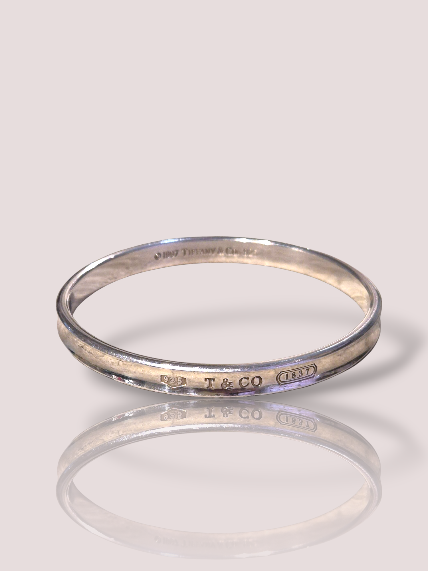 De Vintage Tiffany & Co '1837' zilveren gesloten armband, is een elegant sieraad dat elke outfit verfijnt. Deze zilveren armband, die tot de categorie JEWEL behoort en specifiek een BRACELET is, draag je het beste solo of in combinatie met andere delicate sieraden voor een subtiele, tijdloze look. Perfect voor zowel dagelijks gebruik als speciale gelegenheden.