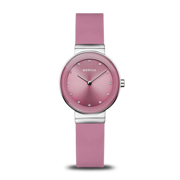  Dit speelse en toch elegante dameshorloge uit de Classic collectie van BERING brengt kleur in het spel &ndash; zonder in te leveren op verfijning. De zachte roze wijzerplaat met fijne sunray-afwerking vangt het licht in subtiele stralen en geeft het ontwerp een vrouwelijke diepte. Twaalf sprankelende kristallen indexen accentueren de strakke lijnen en zorgen voor een subtiele schittering.  De ronde kast van 29 mm in glanzend zilverkleurig roestvrij staal past perfect bij de soepel vallende siliconen band in een bijpassende roze tint. Het materiaal voelt comfortabel aan op de huid en sluit met een klassieke gesp &ndash; stijlvol voor dagelijks gebruik en licht om de pols.  Het platte saffierglas beschermt het delicate oppervlak betrouwbaar tegen krassen, terwijl het nauwkeurige quartz uurwerk binnenin zorgt voor een exacte tijdweergave. Met een waterbestendigheid van 3 ATM is dit horloge ideaal voor de lichte, alledaagse momenten van het leven. 
