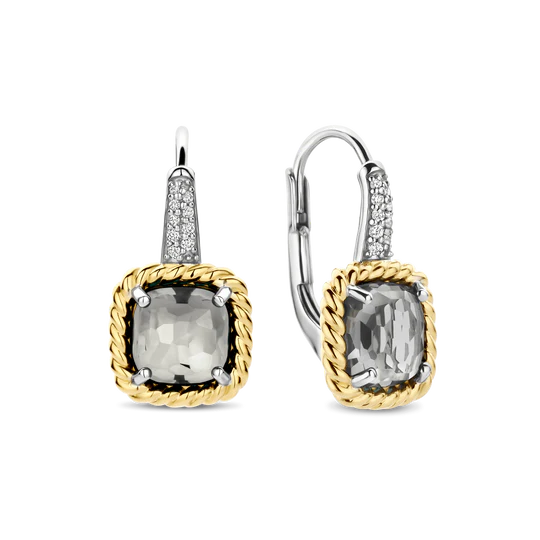 Voeg een vleugje modern erfgoed toe met deze TI SENTO vergulde oorbellen 78042GG. Vervaardigd uit 925 sterling zilver tonen deze leverback oorbellen kussenvormige transparante grijze stenen, fijn gefacetteerd voor een zachte, smoky schittering. Elke steen wordt vastgehouden in een gedraaide goudkleurige klauwzetting, wat structuur en een vintage-geïnspireerde look toevoegt. De platinakleurig vergulde haken zijn pavé gezet met briljant geslepen witte zirconia en bieden een verfijnd contrast van tinten en texturen. Ingetogen maar onderscheidend, ze brengen subtiele allure in zowel dagelijkse outfits als avondlooks. Nikkelvrij en hypoallergeen, ze bieden tijdloze elegantie met draagcomfort de hele dag door.