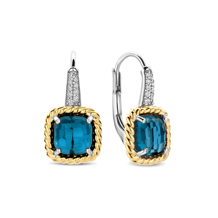 Maak een gedurfd maar elegant statement met deze TI SENTO vergulde oorbellen 78042DB. Vervaardigd uit 925 sterling zilver tonen deze leverback oorbellen levendige transparante donkerblauwe kussenvormige stenen, gefacetteerd om het licht te weerkaatsen met een subtiele gloed. De gedraaide goudkleurige klauwzettingen geven een vintage-geïnspireerde look, terwijl de platinakleurig vergulde haken, pavé gezet met briljant geslepen witte zirconia, een verfijnde fonkeling en contrast toevoegen. Hun sculpturale vorm en diepe kleur brengen diepte en karakter in elke look. Nikkelvrij en hypoallergeen, deze oorbellen bieden de hele dag comfort en tijdloze schittering.