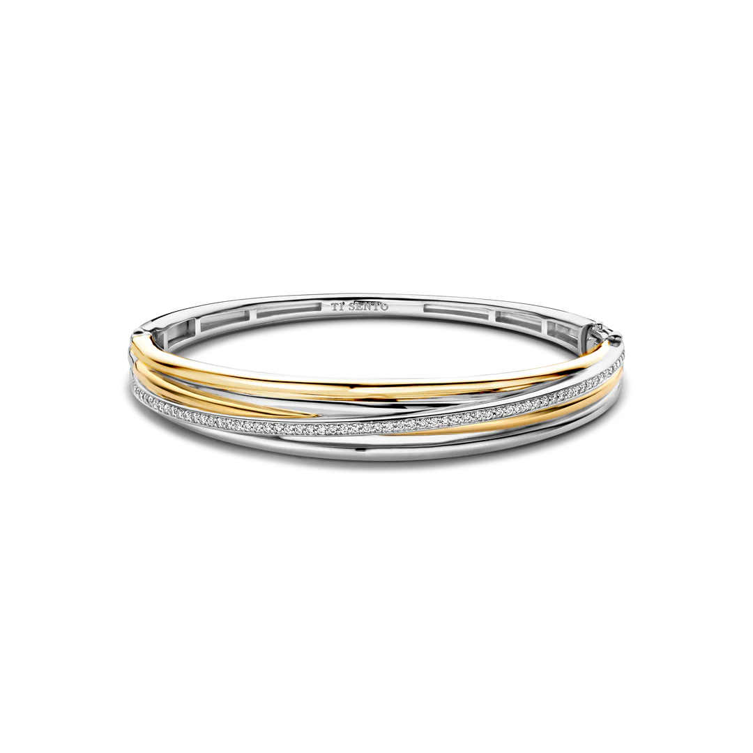 Ervaar de luxe geïnspireerd door vintage met deze TI SENTO vergulde zilveren bangle armband 23046ZY. Gemaakt van 925 sterling zilver en bedekt met platina voor een blijvende schittering, beschikt dit gedurfde statementstuk over drie slanke banden. De centrale band is bedekt met geelgoud, wat een vleugje stralende luxe aan het ontwerp toevoegt. Een vierde band, gedecoreerd met een fonkelende pave van witte cubic zirconia-stenen, kruist de andere banden en creëert een betoverende samensmelting van licht en schaduw. Geïnspireerd door de verfijnde details van architectonische structuren, is deze armband een eerbetoon aan modern design. 