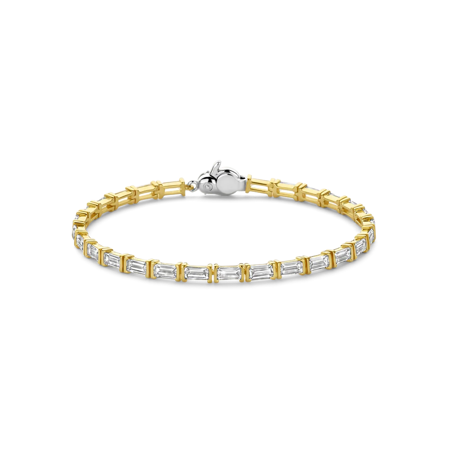 Ervaar ultieme luxe met deze TI SENTO vergulde zilveren tennisarmband 23041ZY, een meesterwerk van verfijning en glamour. Gemaakt van 925 sterling zilver en verguld beschikt deze armband over een sprankelende rij van smaragdgeslepen witte cubic zirconia stenen. De warme gloed van het goud voegt een vleugje luxe toe aan het betoverende ontwerp. Deze armband is een moderne interpretatie van een klassiek stijl, perfect voor de vrouw die een gedurfde indruk wil maken. De veelzijdigheid zorgt ervoor dat het sieraad moeiteloos van dag naar avond overgaat, en voegt een vleugje luxe toe aan elke outfit. Verrijk je dagelijkse look met dit verbluffende stuk. Draag het alleen voor een gedurfde uitstraling of stapel het met andere TI SENTO armbanden voor een samengestelde ensemble die vintage-geïnspireerde charme uitstraalt. Vakkundig vervaardigd voor gevoelige huiden, zorgt deze nikkelvrije en hypoallergene armband voor blijvend comfort en kwaliteit.