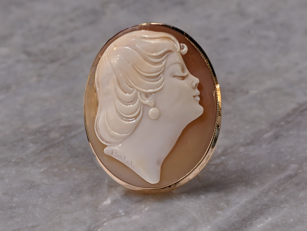 18 Karaats Geel Gouden Vintage Broche met een met de hand geslepen camee schelp.
Aan de achterzijde vindt u een aanhechting voor een optie om de broche tevens als hanger te kunnen dragen.
De speld sluiting heeft een veiligheid oog. 