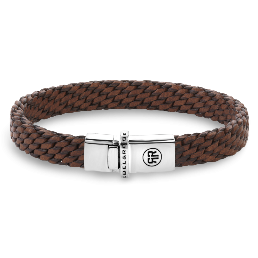 De Mastery Collection - Woven Patina Gognac is 9,2 mm breed en de sluiting is gemaakt van 925 Sterling Silver. Deze armband maakt deel uit van de Mastery Collection: dit zijn handgemaakte, exclusieve sieraden, die op een unieke en zeer arbeidsintensieve manier zijn gemaakt. De Mastery Collection van Rebel & Rose is een bijzondere serie handgemaakte armbanden van 8 gevlochten strengen van 2 mm breed. De kern van het vlechtwerk bestaat uit &eacute;&eacute;n leren koord. Het maken van deze armbanden is complex en zeer arbeidsintensief. Een geoefende vlechter kan er drie per dag maken. Na het vlechten worden de banden in water behandeld, geperst, gedroogd, weer nat gemaakt, gerold, geperst en vervolgens gewaxt en weer gedroogd. In totaal duurt de afwerking nog 3 dagen. Behalve in het regenseizoen, dan duurt het langer, want het leer moet buiten drogen. Het resultaat mag er echter zijn: een bijzonder exclusieve armband, die heel comfortabel en soepel is om te dragen.