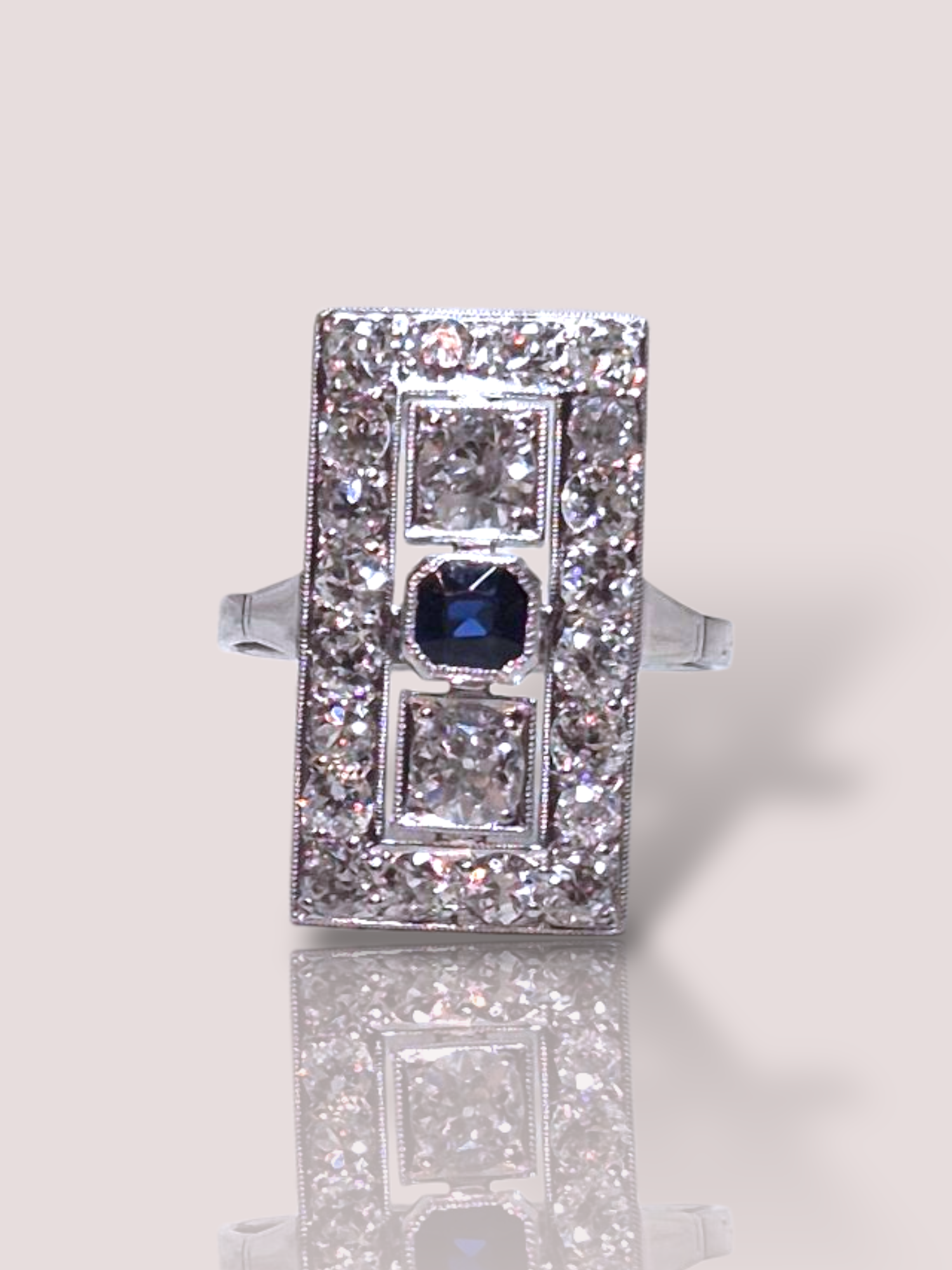 Deze Art-Deco 14k witgouden en platina ring is een verfijnd sieraad met schitterende diamanten en een diepe, blauwe saffier. Perfect voor speciale gelegenheden of als opvallend accessoire bij alledaagse outfits. Draag deze ring solo voor een elegante look of combineer met andere sieraden voor extra glamour. 

De ring bevat 20 diamanten van elk 0,03ct  H-I en SI2-P1 kwaliteit en 2 grotere diamanten van 0,25ct elk die Bolsjewiek geslepen zijn. In totaal bevat de ring 1,10ct aan diamant en in het midden zit een donkerblauwe saffier.