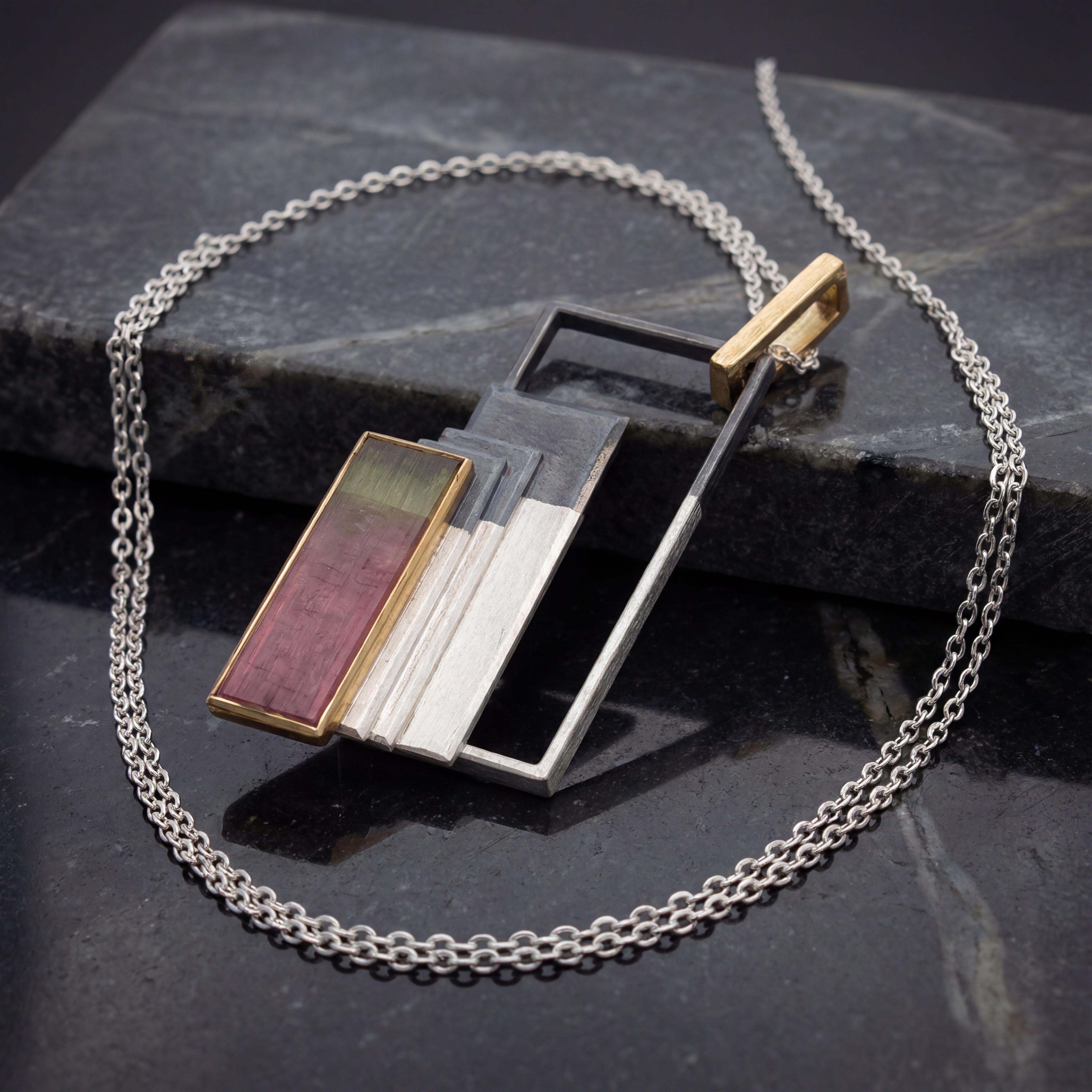 Dieser Anhänger mit einem außergewöhnlichen Turmalinrechteck mit einer scharf abgesetzten natürlichen Farbzonierung bordeaux und grün, ist in Silber und Gold 900 gefertigt. Er besticht durch seine kontrastreiche Materialkombination. Tragen Sie ihn stilvoll an einer feinen Silber- oder Goldkette, um jedem Outfit eine luxuriöse Note zu verleihen. Perfekt für besondere Anlässe und zur eigenen Freude.