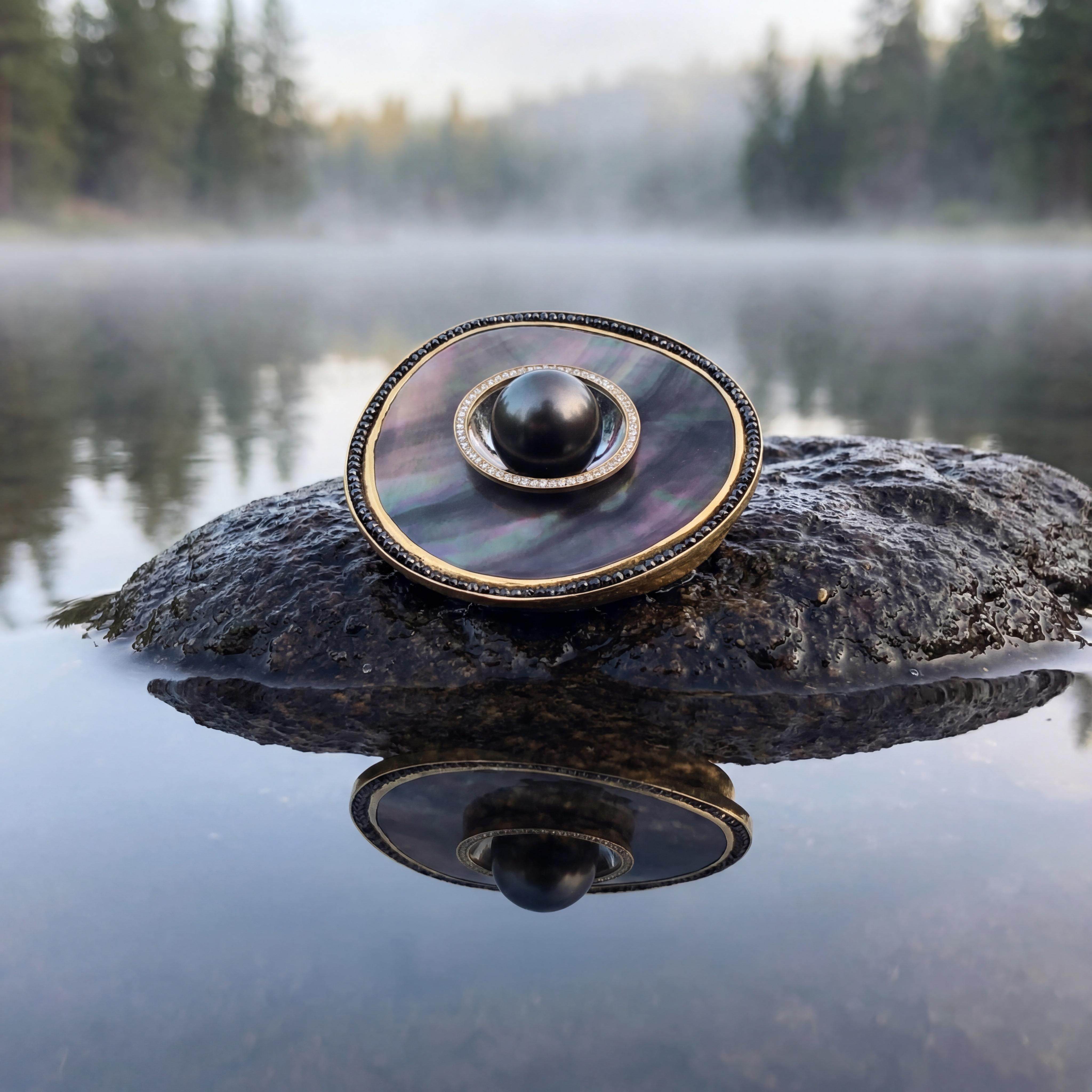 Griechische Tragik, historische Dramatik, künstlerische Perfektion: Die exotische Tahitiperle von herausragender Größe und Qualität steht zurecht im Zentrum dieses einzigartigen Schmuckstücks. Zart gelbgolden eingefasst, umrahmt ein Kreis aus funkelnden Brillanten die Perle, veredelt durch einen Kreis schwarzer Diamanten. Verbunden werden die wertvollen Steine durch die changierenden Aspekte der eindrucksvollen Permuttscheibe. So facettenreich die visuelle Interpretation, so vielfältig die Funktionen: als Ansteckschmuck, Collier-Schließe oder Anhänger - alle erforderlichen Mechaniken sind unsichtbar vorhanden.

Anhänger in Gelbgold 750, schwarze Diamanten, Perlmuttscheibe, Schale aus Weißgold 750 mit 59 Brillanten 0,563ct G vsi, Durchmesser ca. 80 mm.

Gefertigt im Atelier Kissner
Design: Carsten Kissner