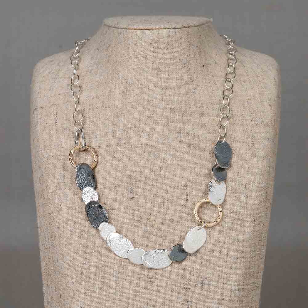 Collier gemaakt van drie verschillende materialen: 925 sterling zilver, geoxideerd zilver en Goldfilled. Dankzij de schakeltjes kan dit collier op meerdere lengtes worden gedragen, met een maximale lengte van 46 cm. Het tijdloze ontwerp maakt het perfect te combineren met bijpassende oorbellen, een ring en een armband voor een complete en stijlvolle look.