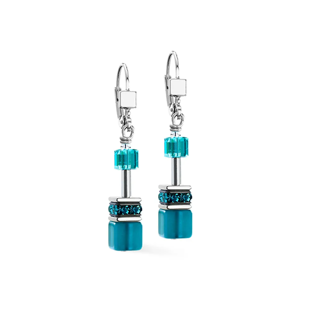 De betoverende allure van de GeoCUBE Iconic Teal oorhangers 40 mm, een juweel van vakmanschap van het merk Coeur de Lion. Deze prachtige oorhangers zijn een verfijnde combinatie van tijdloze elegantie en moderne flair. Met een subtiele zilverkleurige afwerking en een lengte van 40 mm stralen ze door de precieze afwerking in edelstaal. De sprankelende blauwe steentjes, gemaakt van Swarovski en Strass, geven een onweerstaanbare schittering die elke look naar een hoger niveau tilt.