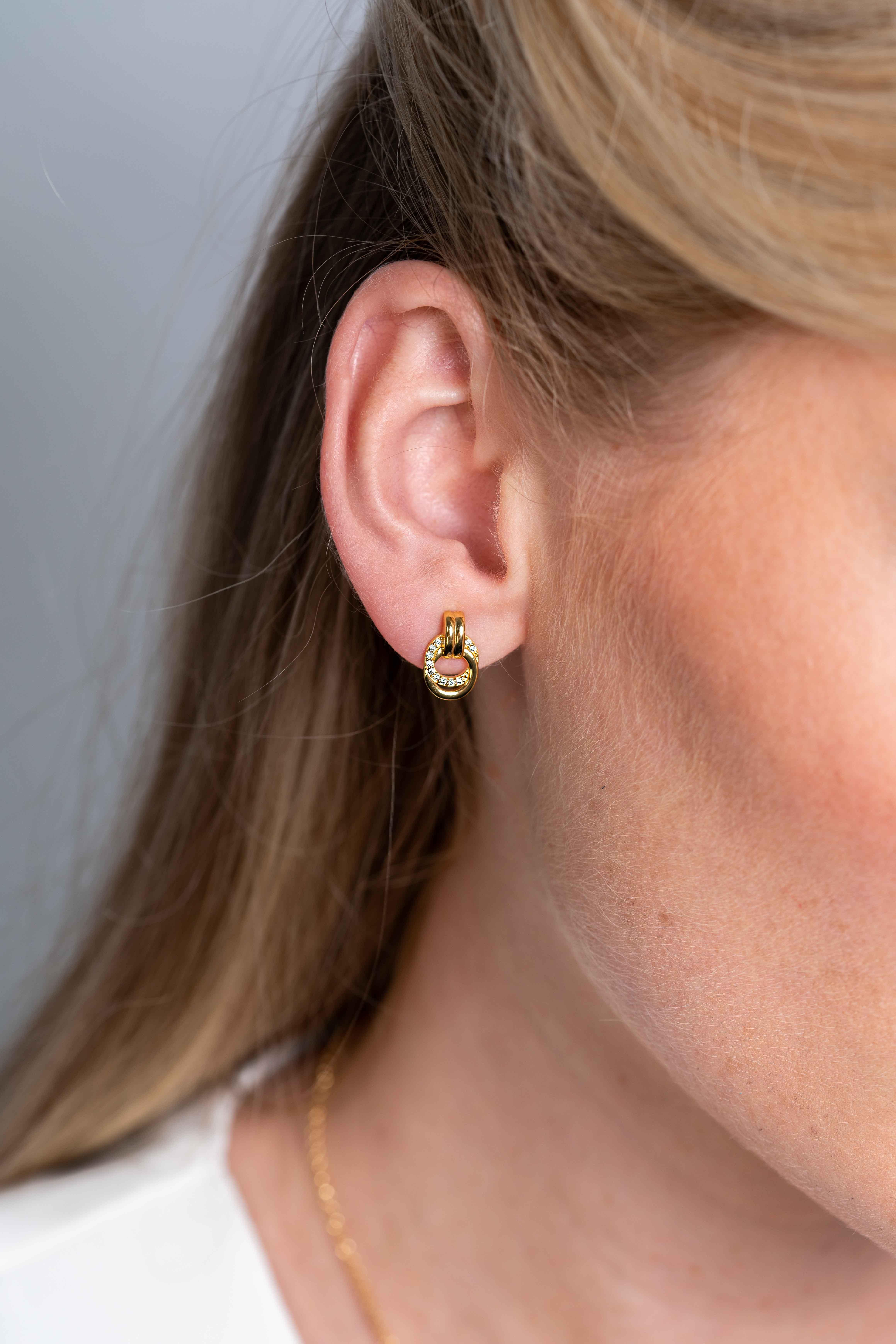 ZINZI zilveren oorstekers 13mm in 14K geelverguld met twee verbonden open rondjes, glad en bezet met witte zirconia's. Deze oorknoppen zijn stijlvol en elegant bij elke outfit! Vervaardigd van eerste gehalte zilver (925) en voorzien van een extra 14K geelgoudkleurige laag.