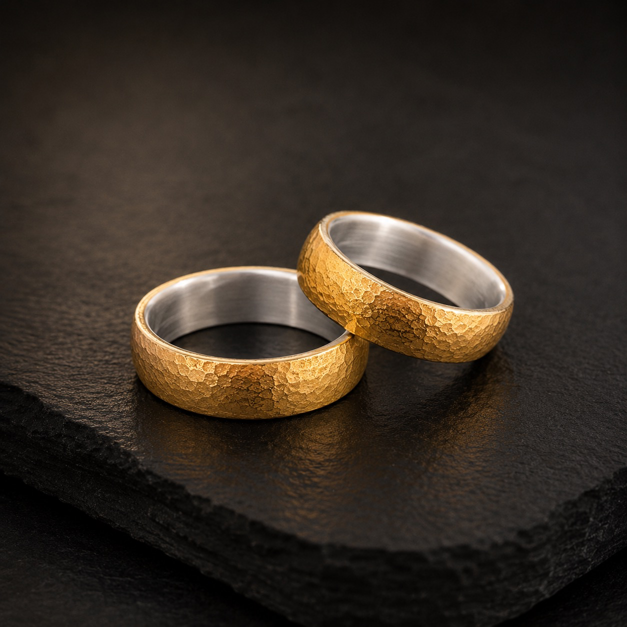 Zwei Ringe. Ein Versprechen. Echtes Handwerk.
Diese au&szlig;ergew&ouml;hnlichen Trauringe verbinden die warme, unverwechselbare Farbe von Feingold 999 mit einem Kern aus Silber. Das Feingold ummantelt den Ring und verleiht ihm seinen charakteristischen, besonders satten Goldton. Im Inneren bleibt das Silber sichtbar &ndash; ein spannender Bicolor-Kontrast, der die handwerkliche Konstruktion bewusst zeigt.
Die lebendige Oberfl&auml;che entsteht durch die Bearbeitung von Hand. Jeder Hammerschlag hinterl&auml;sst seine eigene Spur und macht jeden Ring zu einem echten Unikat. Kleine Unterschiede sind dabei kein Zufall, sondern Ausdruck der individuellen handwerklichen Fertigung.
Diese Trauringe werden ausschlie&szlig;lich handwerklich in unserem Meisteratelier hergestellt &ndash; ohne industrielle Serienfertigung. Vom Aufbau der beiden Edelmetalle &uuml;ber die Formgebung bis zur Oberfl&auml;chenbearbeitung entsteht jedes Paar mit Erfahrung, Sorgfalt und viel Gesp&uuml;r f&uuml;r das Material.
So entstehen Trauringe, die nicht vollkommen gleich sein m&uuml;ssen, um vollkommen zusammenzugeh&ouml;ren.
Feingold 999 & Silber. Zwei Materialien. Zwei Ringe. Eine Verbindung f&uuml;rs Leben.