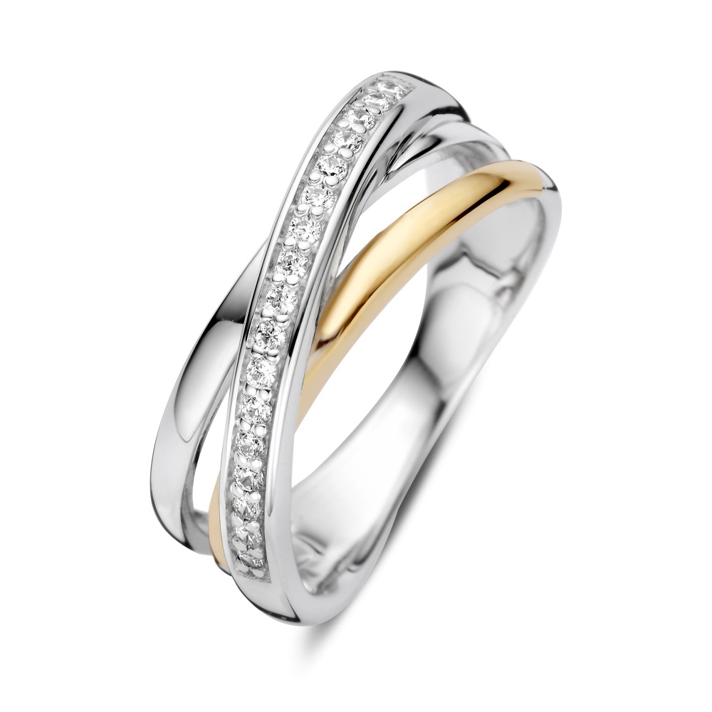 Deze luchtige cross-over ring van zilver met 14 karaat goud wordt gevormd door drie sierlijk kruisende banen. De afwisseling tussen gladde lijnen en sprankelende zirkonia&rsquo;s geeft het ontwerp een speels en verfijnd karakter. Een elegante zilveren ring met goud die door de open vormgeving licht en stijlvol oogt.