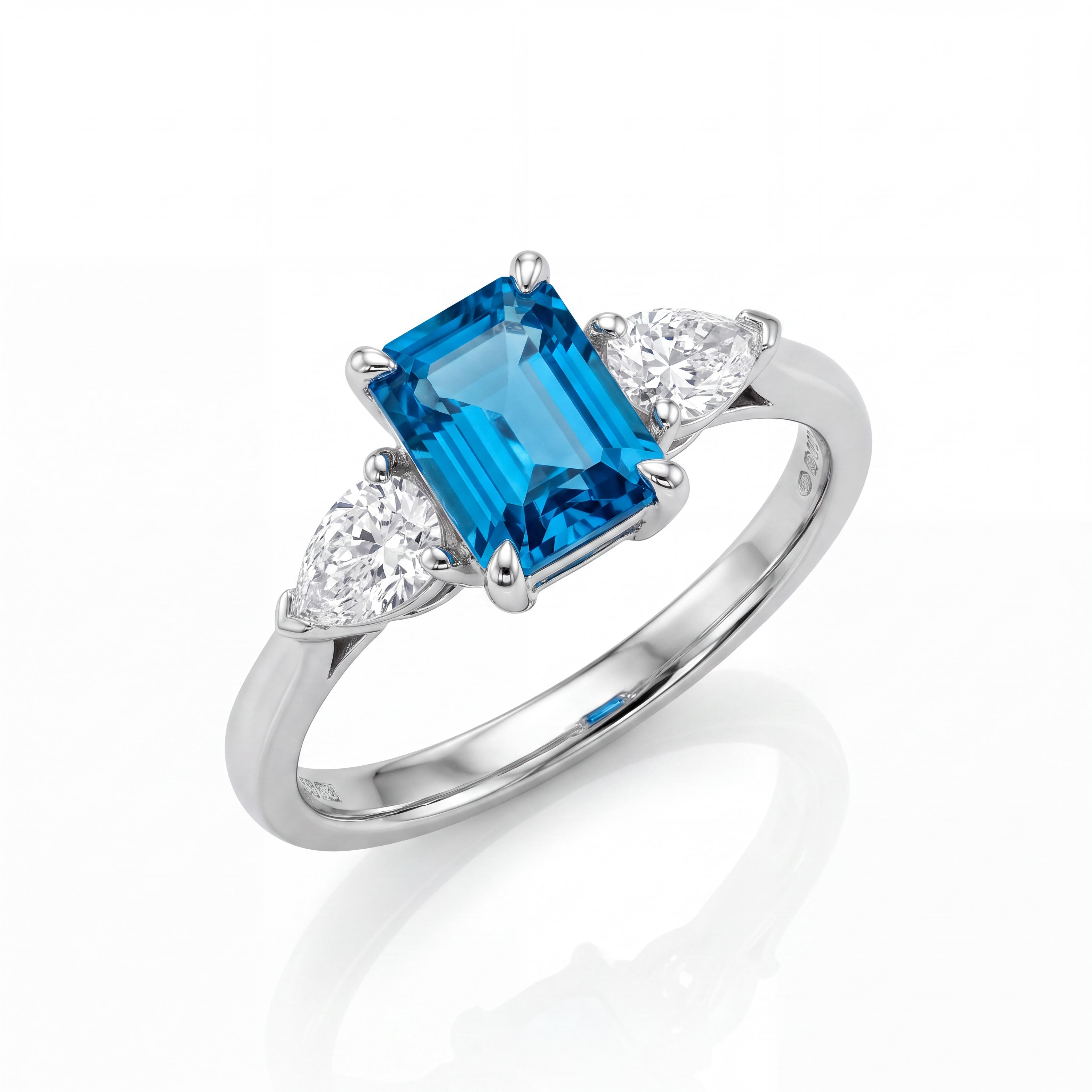 Exclusieve 14 karaat witgouden verlovingsring met een rechthoekig emerald cut London Blue Topaas (0.80 ct), geflankeerd door twee peervormige diamanten (0.30 ct SI1/G). Een koninklijk sieraad uit de eigen collectie van Juwelier Rijk aan de Heiligeweg 10 in Amsterdam.