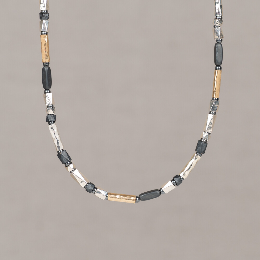 Dit collier uit de Touch of Gold collectie combineert hoekige ronde buisjes met een vierkante Hematiet. Het materiaal bestaat uit 925 sterling zilver, geoxideerd zilver en Goldfilled. De combinatie van materialen geeft het collier een robuust karakter. Hematiet is een donkere steen met een grijze tot zwarte kleur, bekend om zijn dichte structuur en kenmerkende uitstraling. Edelstenen zijn natuurproducten; kleur en formaat kunnen afwijken van de afbeelding.