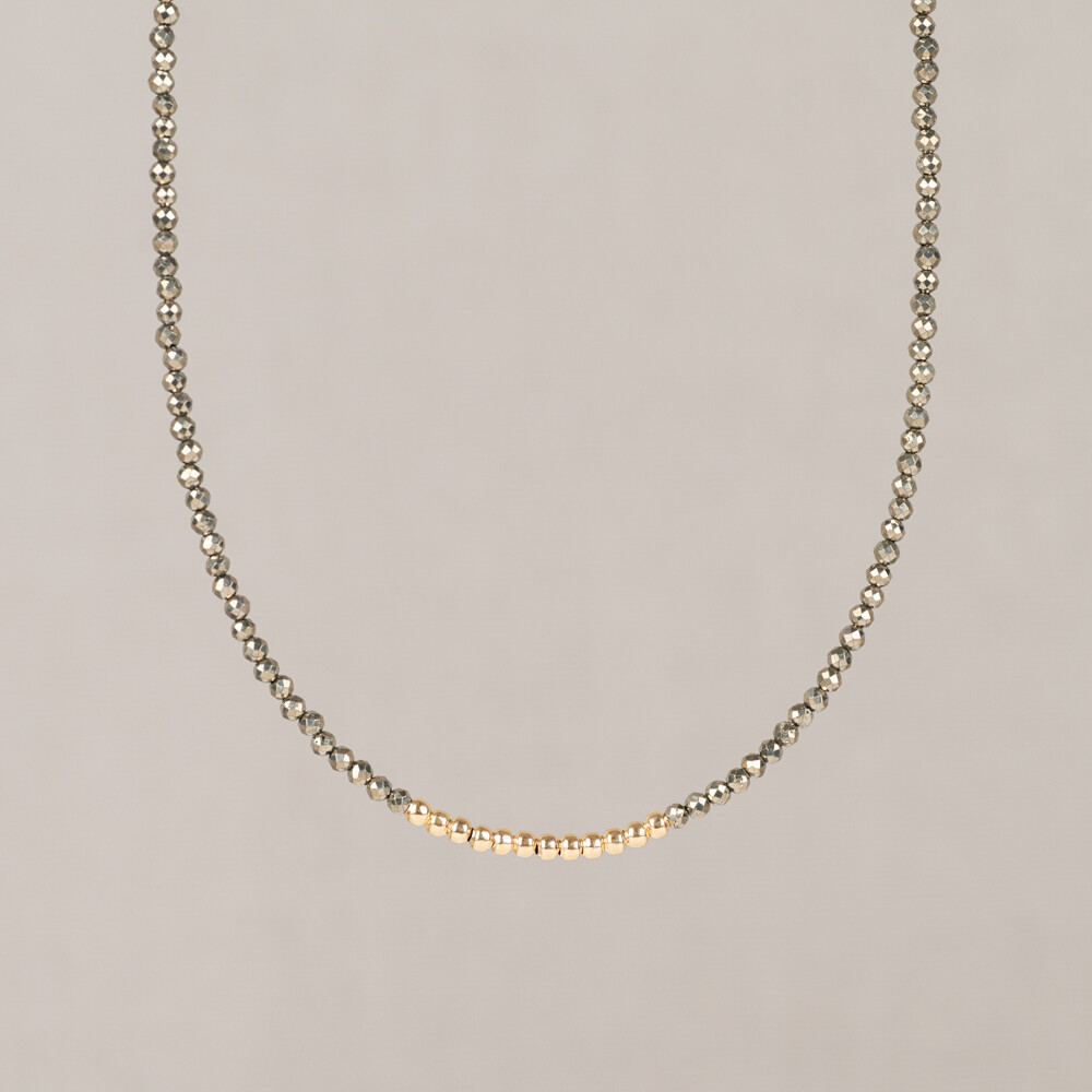 Dit collier is uitgevoerd in Goldfilled en is voorzien van een Pyriet edelsteen in bruine en grijze tinten. Pyriet is een mineraal dat van nature een sterke glans heeft, wat het een opvallende steen maakt in sieraden. De combinatie van Goldfilled en de karakteristieke uitstraling van Pyriet geeft het collier een feestelijk karakter dat past bij uiteenlopende gelegenheden. Het collier maakt deel uit van de Mix & Match collectie, waardoor het goed te combineren is met andere stukken uit dezelfde lijn. Het ontwerp is semi handmatig tot stand gekomen: elk stuk begint als handwerk en wordt vervolgens verder verfijnd. Edelstenen zijn natuurproducten; kleur en afmeting kunnen afwijken van de afbeelding.