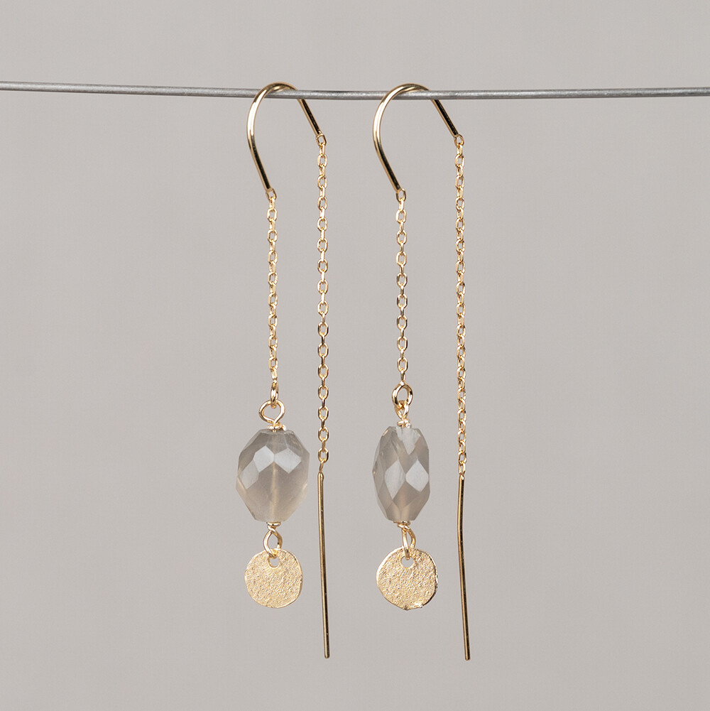 Deze doortrek oorbel is uitgevoerd in verguld zilver en heeft een U-vorm in het midden die zorgt voor een comfortabele, stabiele pasvorm. Aan het uiteinde hangt een organische cirkel, een kenmerkend detail dat de oorbel zijn herkenbare karakter geeft. De oorbel is afgewerkt met een grijze maansteen. Maansteen is een veldspaatstof met een kenmerkende glinstering die adulariscentie wordt genoemd. De kleur en het uiterlijk van de steen kunnen per exemplaar licht vari&euml;ren, omdat maansteen een natuurlijk product is. De kleur van de steen in dit model is grijs. Edelstenen zijn natuurproducten; kleur en afmeting kunnen afwijken van de afbeelding. De oorbel maakt deel uit van de Mix & Match collectie, waardoor hij goed te combineren is met andere stukken uit dezelfde lijn. Het ontwerp is tot stand gekomen via een combinatie van handwerk en een mal, zoals gebruikelijk bij de sieraden van Jeh Jewels.