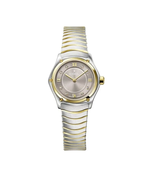 damespolshorloge van Ebel, model Sport classic mini. De wijzerplaat heeft een mooie taupe kleur met 8 briljant geslepen diamanten indexen (0,031 ct) zorgen voor een subtiele, elegante schittering en heeft goudkleurige wijzers. De kast met een diameter van 24 mm is uitgevoerd in edelstaal en verfijnd met accenten van 18 karaat geelgoud, die ook terugkomen in de schroeven en de band. 