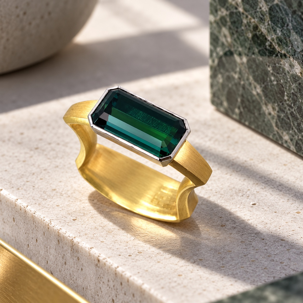 GR&Uuml;NER TURMALIN &ndash; ZEITLOSE ELEGANZ IN KLARER FORM

Ein ausdrucksstarkes Schmuckst&uuml;ck zwischen moderner Architektur und traditioneller Goldschmiedekunst.

Im Mittelpunkt dieses au&szlig;ergew&ouml;hnlichen Rings steht ein tiefgr&uuml;ner Turmalin im eleganten Baguette-Facettenschliff. Seine klaren Linien und faszinierenden Farbnuancen verleihen dem Edelstein eine besondere Tiefe und lebendige Ausstrahlung.

Die skulpturale Ringschiene aus warmem, mattiertem Gelbgold bildet einen spannenden Kontrast zur k&uuml;hlen, geradlinigen Fassung des Turmalins. Flie&szlig;ende Formen treffen auf geometrische Pr&auml;zision &ndash; ein harmonisches Zusammenspiel von Spannung, Leichtigkeit und Eleganz.

Ein Ring mit unverwechselbarem Charakter, der durch seine reduzierte Gestaltung und au&szlig;ergew&ouml;hnliche Formensprache besticht.

Modern. Individuell. Ausdrucksstark.

Ein Schmuckst&uuml;ck f&uuml;r Menschen, die das Besondere lieben und zeitloses Design sch&auml;tzen.