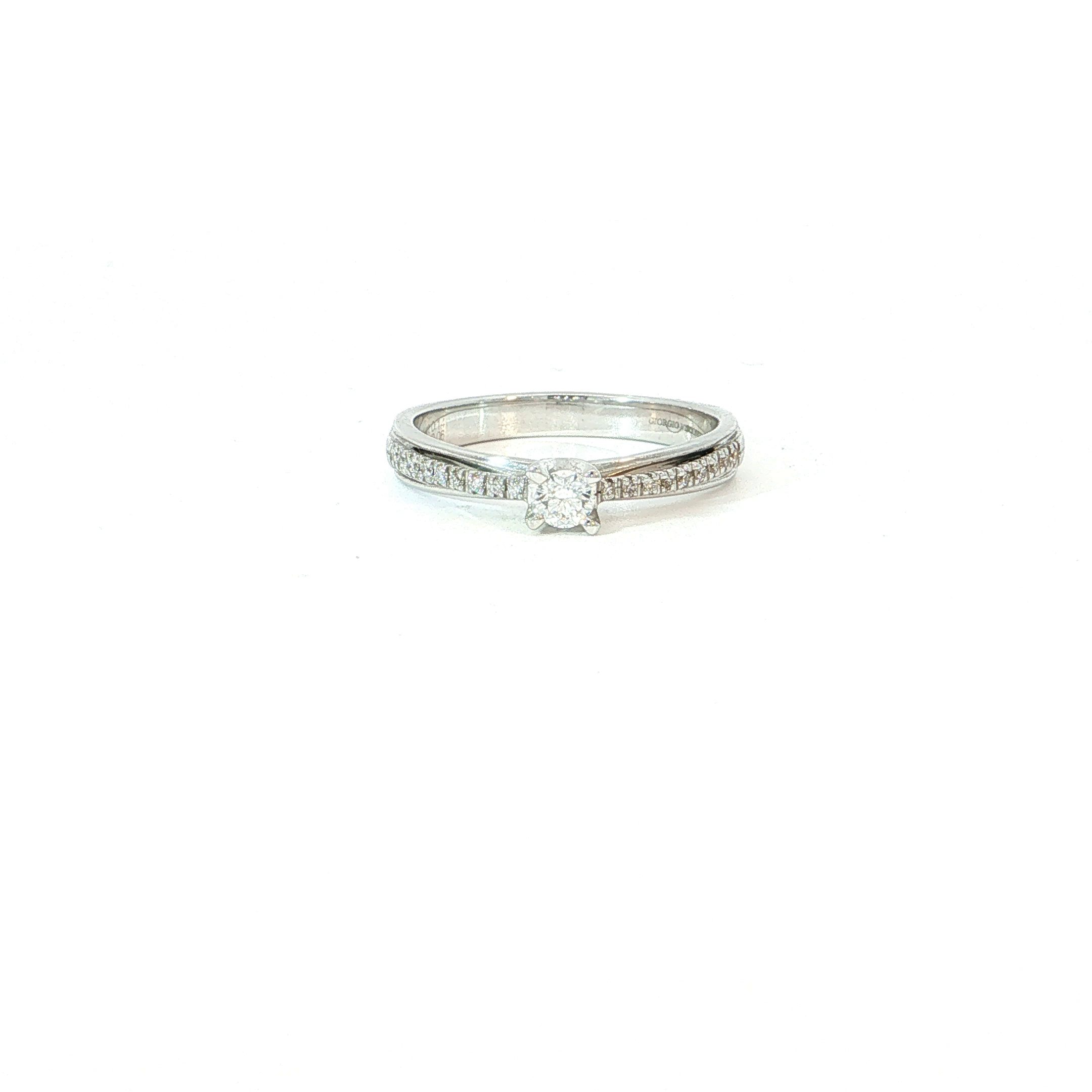 Een klassieker met extra pr&eacute;sence. Deze elegante ring in 18 karaat witgoud combineert een schitterende centrale briljant met een verfijnde rij diamanten die zich langs de ringband uitstrekt. Zo ontstaat een rijk lichtspel dat de middensteen optisch nog sterker naar voren brengt. De fijne afwerking houdt het geheel vrouwelijk en elegant, terwijl de extra diamanten voor n&eacute;t dat tikkeltje meer luxe zorgen. Perfect als verlovingsring, maar even mooi als bijzonder jubileumgeschenk. Voor wie houdt van een klassieke solitair, maar dan met wat meer glamour.